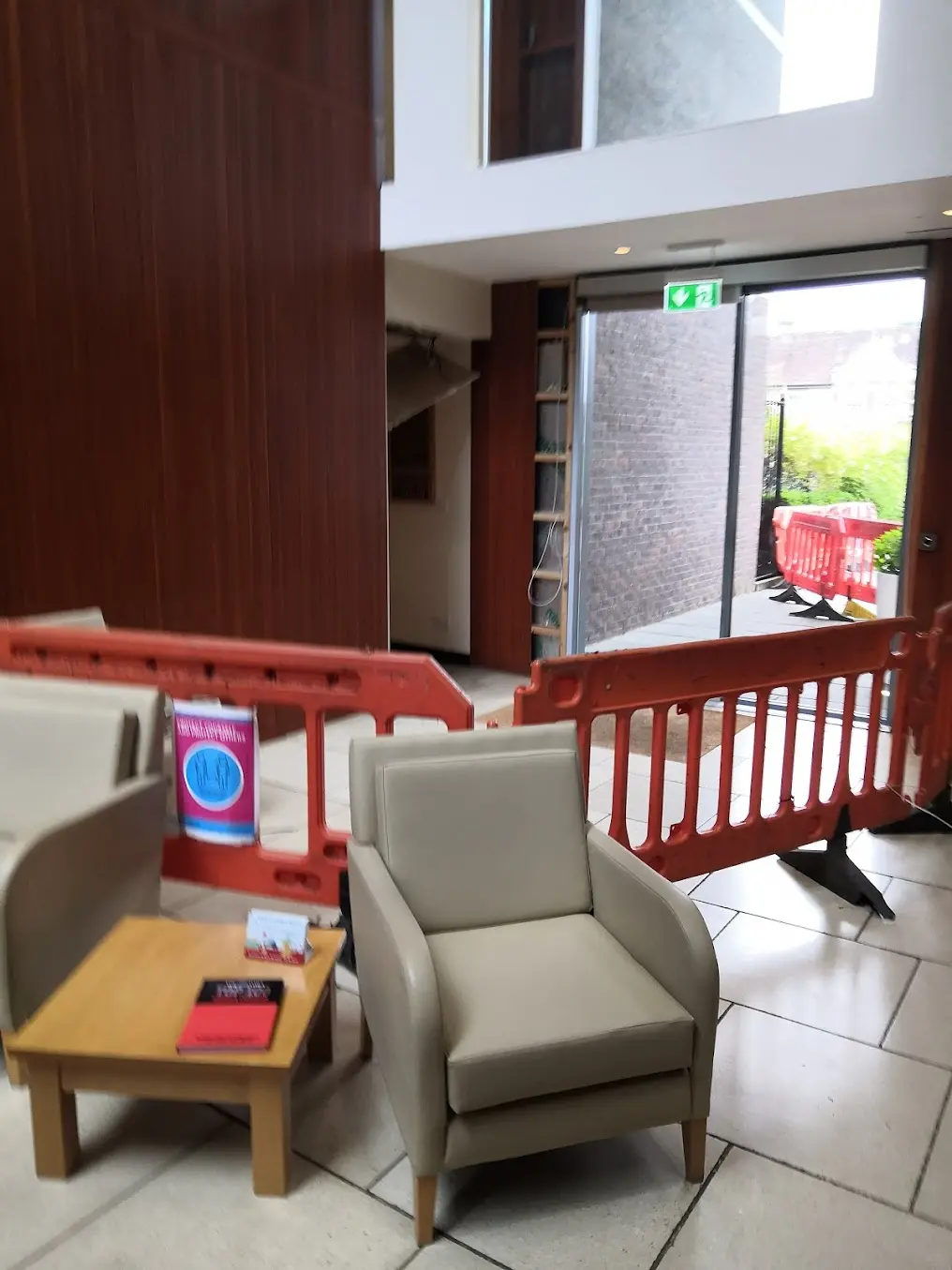 A blurry picture of the broken door in Fitzwilliam: one of the door panes is missing, and the area is surrounded by red barriers. There is a social distancing sign on one of the barriers, but it is too blurry to read.